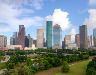 Fototapeta premium A vibrant daytime view showcases the impressive skyline of Houston, Texas, framed by lush greenery and a bright blue sky with scattered clouds.