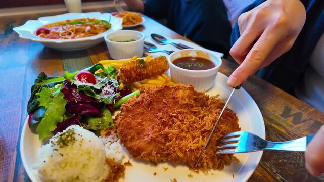 Woman's hands using kitchen knife and tongs to cut a crispy, deep-fried Japanese pork cutlet tonkatsu