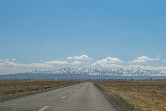 Straight asphalt road leading to the Altai Mountains under a blue sky, Mongolia