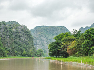 Fototapeta premium Stunning river views in Ninh Binh, Vietnam. Scenic travel and adventure concept. Ideal for tourism, nature, and cultural exploration content. Peaceful escape with lush greenery and serene waters