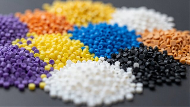Piles of colorful recycled plastic granules arranged in a circular pattern on dark surface, showcasing vibrant hues and textures.