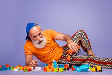 Obraz premium Elderly man in orange shirt with striped pants plays with colorful blocks on a purple background, capturing a playful, carefree moment