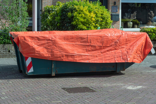 Roll-off container covered with an orange tarpaulin stands outside on the street