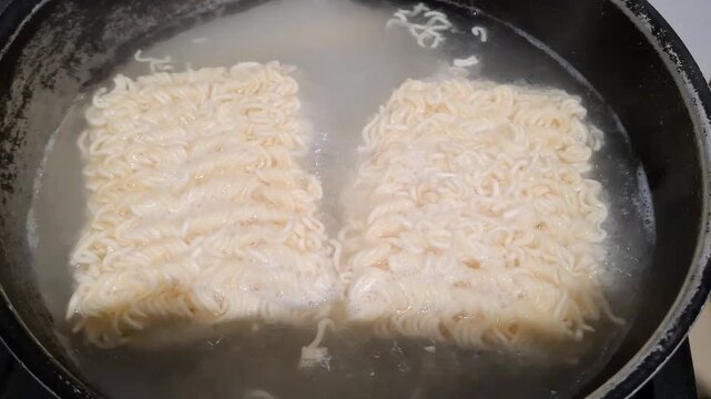 Boiling two blocks of dry instant noodles in hot water. Close-up video of quick cooking process. Perfect for Asian food, easy recipe, or student meal concepts. Stock footage