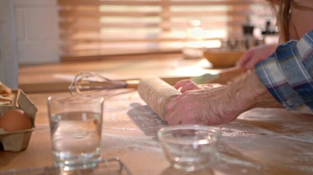 Close-up hands of a chef using a rolling pin to make cookies, with sunlight shining in the background on a morning
