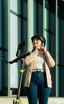 Happy businesswoman buckling helmet on electric scooter for urban commute