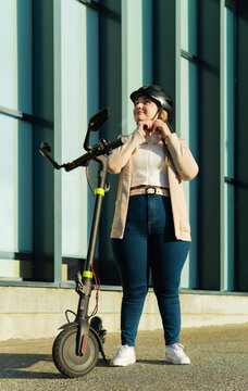 Beautiful woman puts on her helmet after a long day of work on an electric scooter.