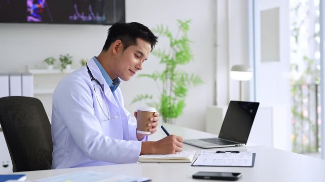 Professional doctor holding a hot coffee drink cup.doing paperwork checking medical documents at workplace. Concentrated physician reading medic form analyzing patient diagnosis or report in hospital.