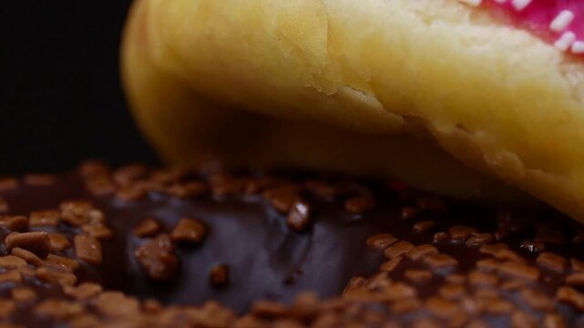 A mouth-watering close-up of two delicious donuts, one chocolate with sprinkles and one pink glazed, stacked on each other.