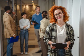 Redhead woman holding clipboard smiling in office hallway © Miljan Živković