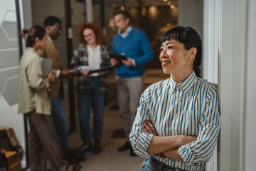Obraz premium Confident asian businesswoman smiling while leaning in modern office space