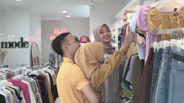 Woman in headscarf browsing colorful racks while friend and companion lift garments, neon hello gorgeous glows in background, rows
