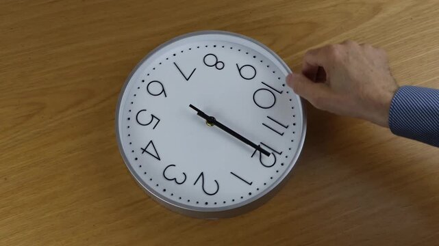 A man's hand turns the clock face, moving the hands