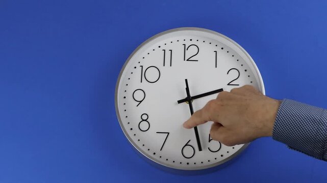 Change the time clocks hour 3 to hour 2. Man's hand moves the hand to change the time, on blue background