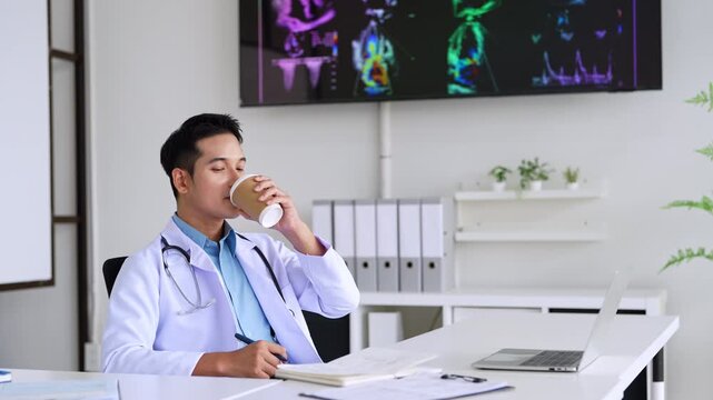 Professional doctor holding a hot coffee drink cup.doing paperwork checking medical documents at workplace. Concentrated physician reading medic form analyzing patient diagnosis or report in hospital.