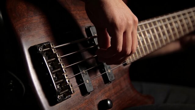 Close-up of Musician's Hand Plucking Strings on a Natural Wood Electric Bass Guitar