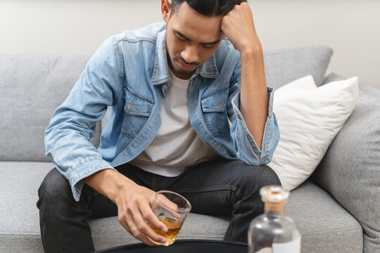melancholy young Asian man drinks alcoholic whisky alone at home feeling dizzy after drunk