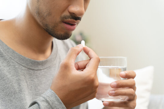 Young man taking painkiller and drink water to healing from cold flu.
