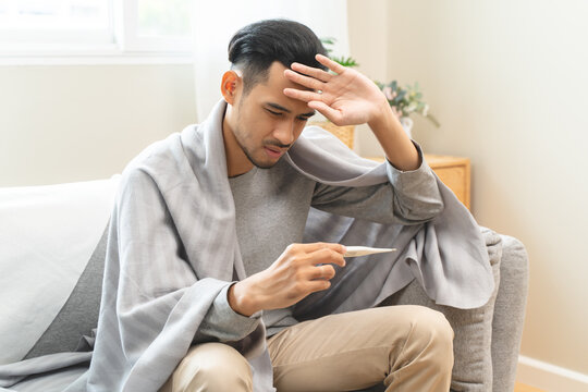 Seasonal cold sickness in people concept, Sick asian man looking at thermometer during measuring his body temperature feel exhausted and headache from fever.