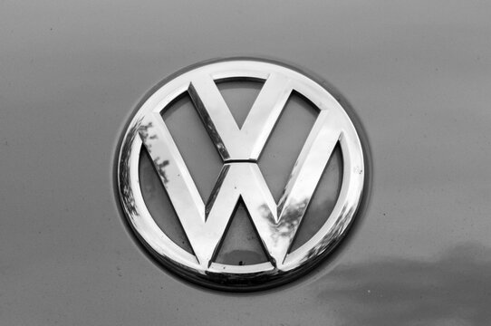 Macro shot of a chrome Volkswagen emblem badge mounted on the grey painted metallic body of a car.