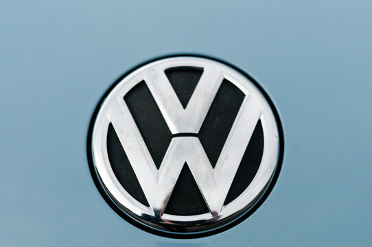 Macro shot of a chrome Volkswagen emblem badge mounted on the light blue painted metallic body of a car.