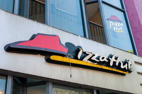 Exterior view of a broken Pizza Hut sign featuring the iconic red branding on a neglected, shuttered restaurant building in a commercial area of the United Kingdom