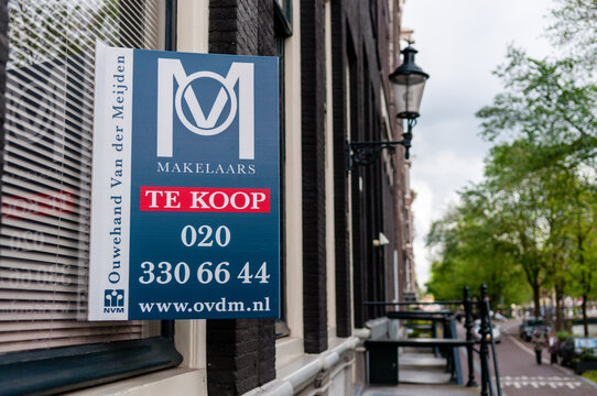 A  "Te Koop" real estate sign mounted on a traditional brick facade window in Amsterdam, signaling a property for sale in the competitive Dutch housing market.