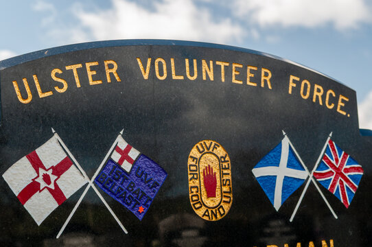 Gravestone of a Ulster Volunteer Force member with flags and the UVF red hand logo