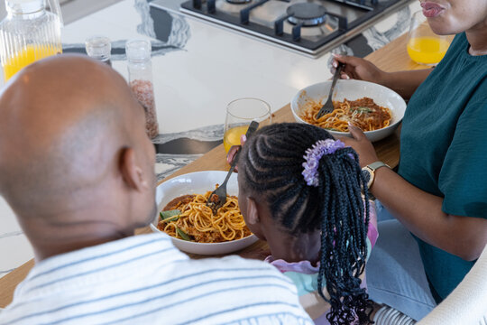 African American family sitting with child at kitchen sharing pasta bowls, forks and juice pitcher
