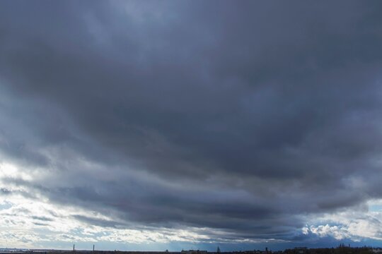 Stormy dark thunderclouds gather in the gloomy sky over the city. Cloudy sky with dark gray rain clouds.