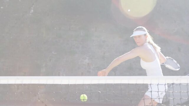 Female tennis pro holding racket swinging backhand returning ball entering above net with sun flare
