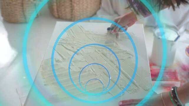 Artist reaching in scraping gesso with knife on canvas, priming ground with teal rings centered