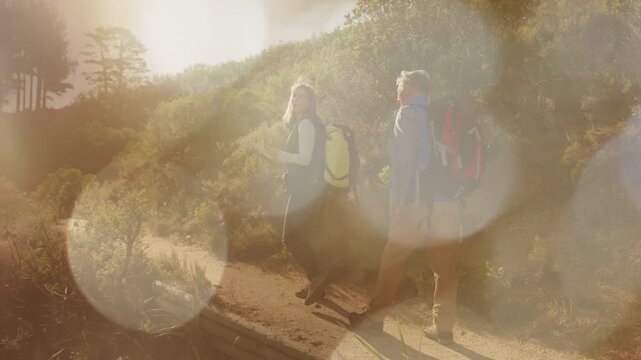 Lead hiker stepping forward, mate following, packs and lens flare partly hiding hikers on hike