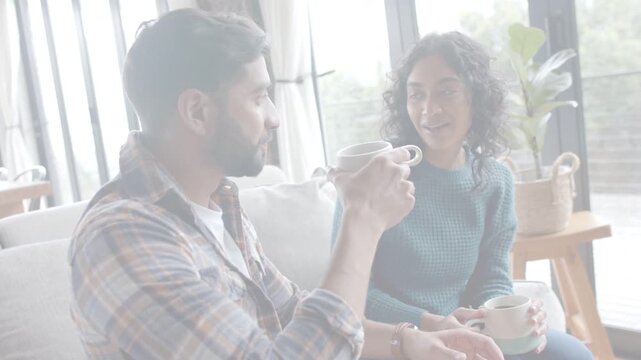 Man sipping mug and sparking woman speaking about health, both gesturing on sofa near windows