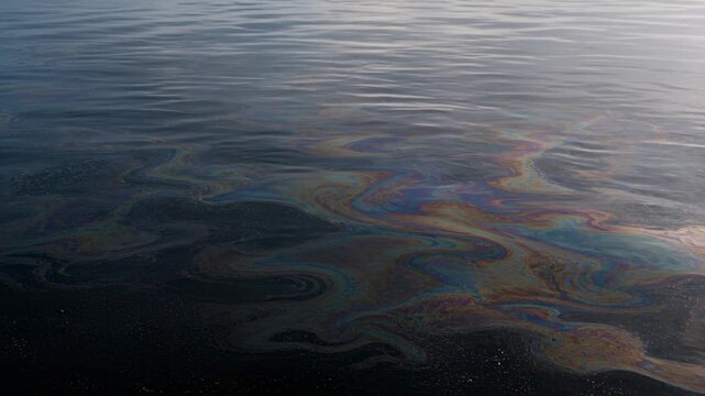 Oil slick spreading across calm water surface with rainbow texture, environmental pollution concept, marine contamination, ecological damage, nature impact.