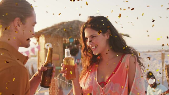 Man with bun and woman with long hair clinking bottles, sparking confetti falling, forming beach ad