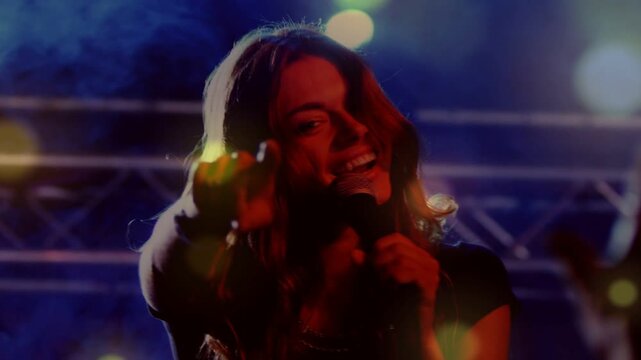 Lead singer stepping into light on music stage, lifting mic, singing, engaging crowd amid bokeh