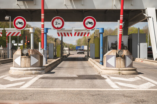 Vehicles approaching toll road payment booths with height restriction signs and barriers, multiple lanes and traffic lights under clear sky, highway logistics and road freight transport concept