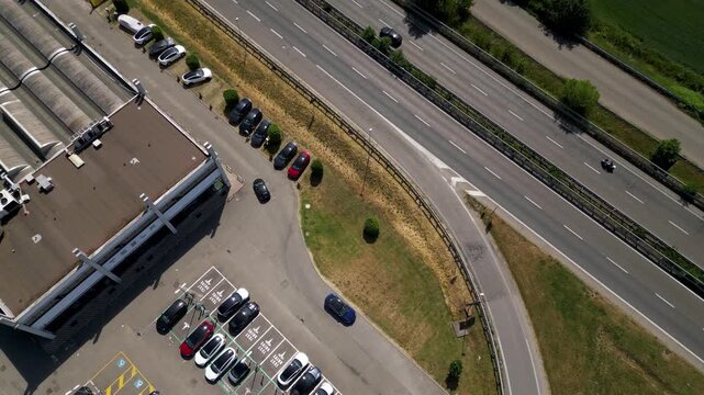 Aerial View of Industrial Area and Highway: An overhead perspective showcases an industrial building complex with a parking lot filled with cars, adjacent to a multi-lane highway with passing traffic.