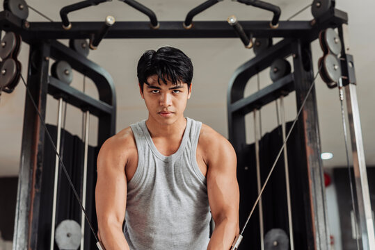 Young Asian man does cable crossover at the gym, holding peak contraction to highlight chest muscle definition and controlled resistance technique.