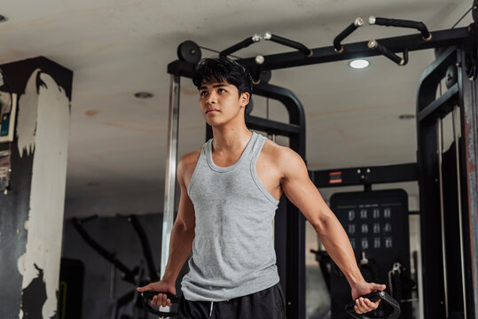 Young Asian man does low cable crossover at the gym, holding bottom position to emphasize lower chest contraction and controlled movement technique.