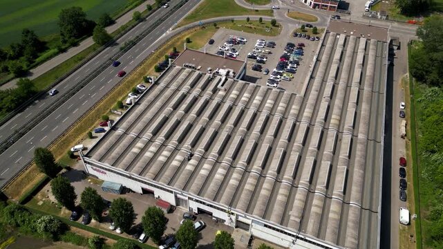 Industrial Complex Aerial View: An aerial perspective showcases a sprawling industrial complex, featuring a large warehouse with a corrugated metal roof adjacent to a busy highway.