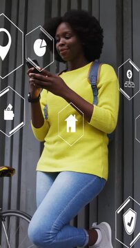Vertical video: Woman leaning on wall, tapping phone causing hex icons appearing, smiling for tech