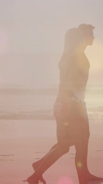 Vertical video: Couple walking along sand, sunset drawing, animated flare tracing shapes for travel