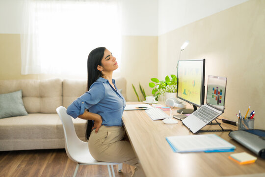 Businesswoman experiencing back pain while working at home, suffering from bad posture and ergonomics