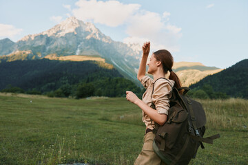 Naklejka premium Cheerful woman hiking outdoors, raising a fist in celebration, wearing a backpack, in a lush valley with distant mountains, bright sky and natural colors