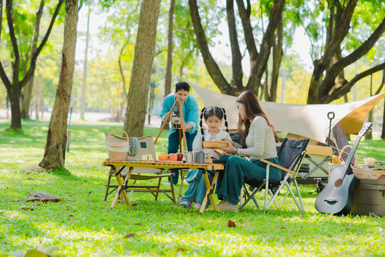 A family of three from Asia enjoyed using their laptops in the park and also enjoyed a picnic together in the park.