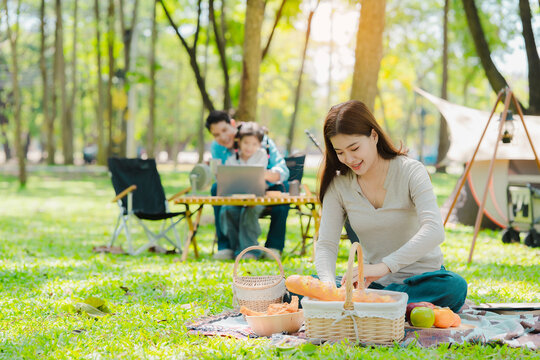 A family of three from Asia enjoyed using their laptops in the park and also enjoyed a picnic together in the park.