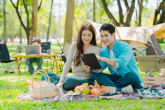 A family of three from Asia enjoyed using their laptops in the park and also enjoyed a picnic together in the park.