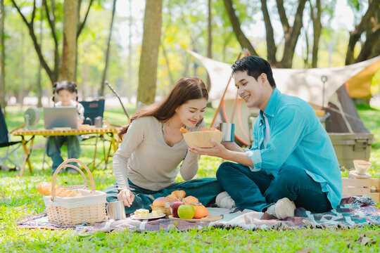 A family of three from Asia enjoyed using their laptops in the park and also enjoyed a picnic together in the park.